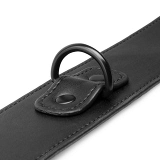 Närbild av Halsband & Handledsbojor: ett svart läderband med en metall-D-ring fäst med två nitar, perfekt som justerbart halsband för spännande BDSM-lekar.