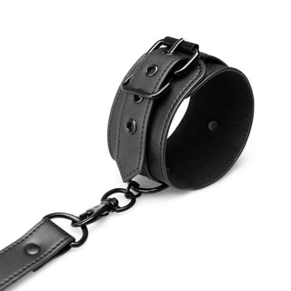 Bondage X-Kors Hogtie har en svart läderhandledsmanschett med metallspänne och en fast kedjerem – perfekt för bondage-set. Visas mot en vit bakgrund.