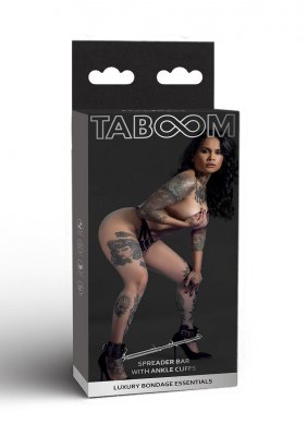 Taboom Bondage Spreader Bar With Ankel Cuffs-lådan innehåller en tatuerad person som hukar i underkläder, håller en spridarbygel och ankelmanschetter. Text betonar de lyxiga bondage väsentligheter som är idealiska för BDSM-lekar.
