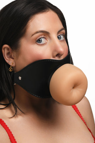 En kvinna i en röd topp bär Ass Face Mun-Gag Beige, som är stor och köttfärgad med en svart rem över munnen.