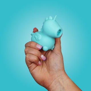 En hand håller Unihorn Mount'n Peak Vibrator, en liten blå enhörningsformad minivibrator, mot en blå bakgrund.
