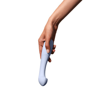 En hand håller i Arc Ice G-punktsvibrator, en böjd, ljuslila vibrator tillverkad av kroppssäkert silikon, mot en vit bakgrund.