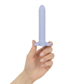 En hand håller Teazers Vagina Dilator Set 4 Delar, med en ljuslila silikon-dilatator med utsvängd bas, perfekt för slidmuskulaturträning och stöd under behandling av vaginism, mot en vit bakgrund.