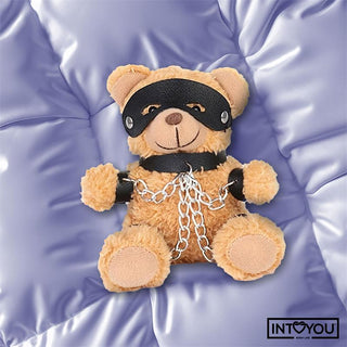 Bubu BDSM Teddy Nyckelring, med svart mask och kedjor, vilar på ett lavendelblankt täcke med INTO YOU-logotypen i hörnet.