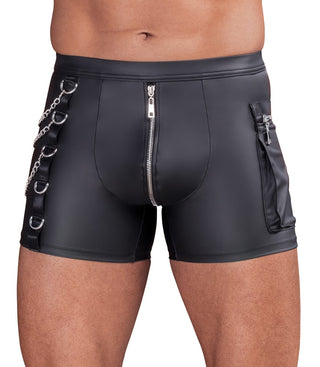 Man klädd i NEK Pants Matt Svart - tajta svarta shorts i läderimitation med blixtlås, kedjor och metallringar, visas från midjan till mitten av låret.