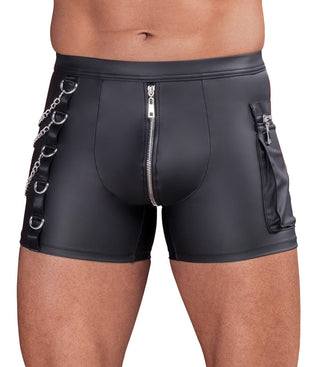 Man klädd i NEK Pants Matt Svart - tajta svarta shorts i läderimitation med blixtlås, kedjor och metallringar, visas från midjan till mitten av låret.
