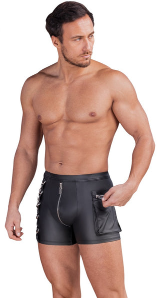 Skjortlös man iklädd NEK Pants Matt Svart - tajta, svarta skinnbyxor med blixtlås - tittar åt sidan och håller i en liten ficka med blixtlås.