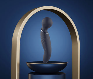 Glam Dual Wand Vibe, tillverkad av elegant svart silikon, visas elegant på ett runt stativ under en böjd metallbåge mot en lugn blå bakgrund, och erbjuder mångsidig massage med sina lugnande vibrationer och eleganta design.