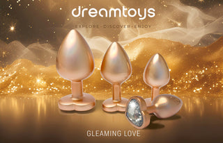 En Pärlguld Buttplugg Large i metallic aluminium med juvelförsedd bas skimrar på en gnistrande guldbakgrund; texten lyder dreamtoys, Gleaming Love.