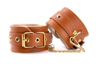 Handbojor Veganskt Läder Cognac handledsmanschetter, designade i brunt veganskt läder med guldspännen och en kopplingskedja, är perfekta för att elegant förbättra din BDSM-kollektion.