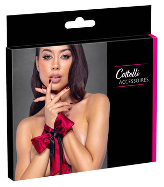 En kvinna med en röd satinbåge på handlederna poserar på en låda märkt "Cottelli Accessoires", där den eleganta Bondage Halsduk visas upp som en snygg bondage-scarfaccessoar.
