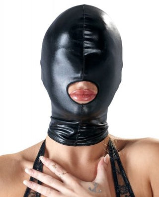 En person som bär BDSM Huva - Bad Kitty - Wetlook-masken i slående svart läder, komplett med en design med öppen mun, täcker sitt ansikte. Deras hand vilar försiktigt på deras bröst, vilket bidrar till den gåtfulla lockelsen.
