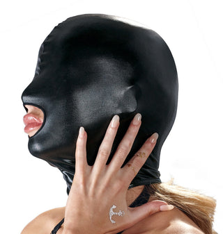 En person i en BDSM Huva - Bad Kitty - Wetlook, rör vid ansiktet med en tatuerad hand, medan det öppna munområdet ger intriger till den glänsande svarta ensemblen.