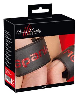 En låda märkt "Badkitty Handbojor - Spank Me" har svarta manschetter med "spank" elegant inskrivet på en, bärs av händerna. Perfekt för dem som utforskar BDSM-lekar.