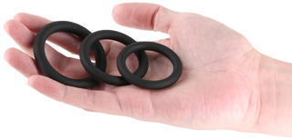 En hand håller tre 3x Stretch Cockrings i silikon i olika storlekar mot en vit bakgrund.