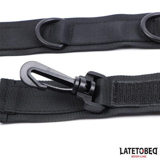 Närbild av en svart nylonrem med plastkrok, metallringar och logotypen LATETO BEG BDSM LINE - perfekt för användning som handledsremmar eller tillsammans med ditt favorithalsband med handledsfästen.