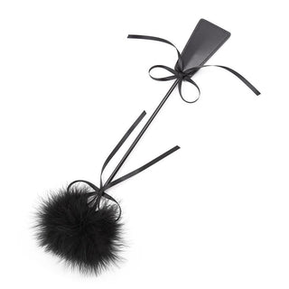Tickler & Paddle 2-i-1 är en paddel i svart läder med handtag, svart rosett och fluffig fjäderpompom – perfekt som en lekfull BDSM-fjäderkitlare för lätta bondage-sessioner.
