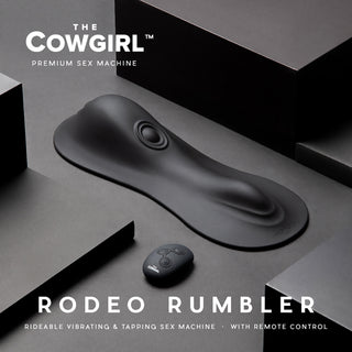 Cowgirl Rodeo Rumbler Ride-On, en svart ride-on-vibrator med fjärrkontroll, erbjuder en handsfree-upplevelse och visas mot en geometrisk svart bakgrund.