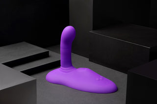 The Cowgirl Rodeo Rider Thrusting, ett abstrakt lila objekt med en böjd upprätt form tillverkad av kroppssäker silikon, sitter på en mörk geometrisk yta.