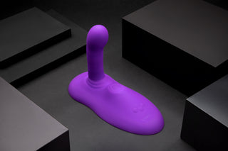 Cowgirl Rodeo Rider Thrusting vuxenleksak, tillverkad av kroppssäker silikon i lila, visas på en mörk yta med svarta rektangulära block runt den.