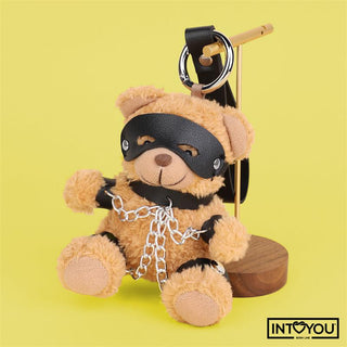 Bubu BDSM Teddy Nyckelring: En plysch teddybjörn med svart mask och veganskt läderkedjor, används som nyckelring, visas mot gul bakgrund.