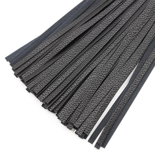 Närbild av flera svarta läderremsor från Latetobed Classic Flogger 42cm, arrangerade i parallella linjer mot en vit bakgrund.