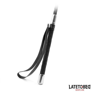 The Svart BDSM Piska 60cm i veganskt PU-läder har eleganta silverdetaljer och en handledsrem. Perfekt för att addera dominans till din samling. Visas mot vit bakgrund.