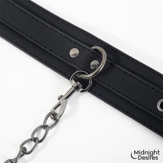 Set med halsband och fotledsband i svart veganskt läder, med kedja, spänne och synlig logotyp.
