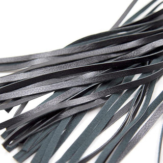 Närbild av flera mjuka remmar från Black Sapphire Vegan Flogger, tillverkad av veganskt läder, liggande på en vit yta.