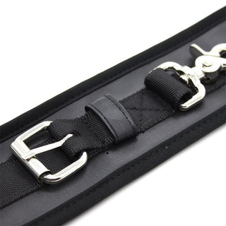 Närbild av Latetobed Handbojor Svart, ett svart nylonband med silverspänne och lås på en vadderad yta - perfekt för bondageentusiaster som söker mångsidiga BDSM-tillbehör.