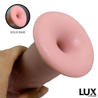 En hand håller Lux Otto Mjuk Dildo 20 cm, en rosa silikonleksak för vuxna med en strap-on-kompatibel, rundad öppen ände och en solid bas.