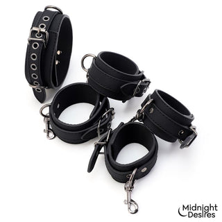 Ett set med fyra svarta handledsbojor i veganskt läder med metallspännen, försedda med Midnight Desires Bondageset-logotypen.