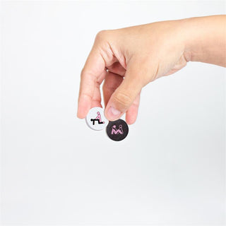 En hand håller två runda pins med abstrakta rosa och svarta mönster på en vit bakgrund, vilket återspeglar den lekfulla kreativiteten hos Fyra i Rad Sexspel Play4Sex, ett roligt sexspel för par.