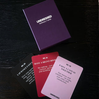 En lila Undressed Intimacy Cards Kortlek box med tre prompt cards for par utplacerade på en mörk yta - idealisk för att stärka relationen.