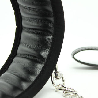 Närbild av Latetobed Justerbart Halsband - ett svart, justerbart BDSM-halsband med en silverkedja och metallspänne - mot en vit bakgrund.