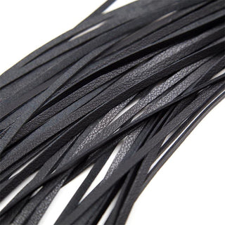 Närbild av flera tunna, svarta läderremsor från Latetobed BDSM Flogger 69 cm, arrangerade mot en vit bakgrund.