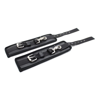 Två Latetobed Handbojor Svart - handledsfästen i svart läder med metallspännen och clips - ligger platt på en vit bakgrund, perfekt för bondagelek.
