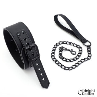 Svart BDSM-halsband i veganskt läder med spänne och fastsatt kedjekoppel, avbildat mot en vit bakgrund.
