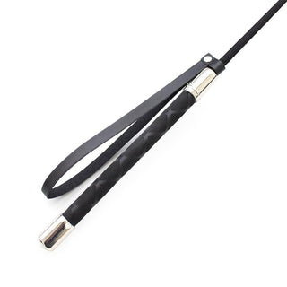 Latetobed Riding Crop 66 cm är en svart crop med en handledsrem med ögla och silverfärgade detaljer, perfekt för BDSM eller dominanslekar, visad på en vit bakgrund.