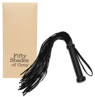 En svart Fifty Shades of Grey Flogger, med ett flätat handtag och handledsrem, ligger bredvid sin beige rektangulära låda.