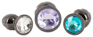 Metall Butt Plug Set har tre metalliska pluggar med ändar i ädelstensstil i klar, lila och blå, arrangerade för att visa upp deras polerade ytor. Perfekt för att utforska anal stretching eller uppleva spänningen med temperaturspel.