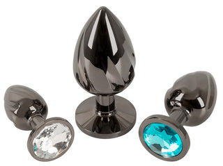 Metall Butt Plug Set innehåller tre svarta metallpluggar. Två mindre har klara och blå ädelstenar, perfekta för temperaturspelskänsla, medan den större pluggen är slät med en reflekterande design som är idealisk för anal stretching.