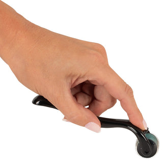 En hand håller ett svart Micro Pinwheel med ett grönt rullhuvud, med små nålar gjorda av rostfritt stål för effektiv hudbehandling. Den kompakta designen visar upp precision, och personen har snyggt klippta fingernaglar med lätt nagellack.