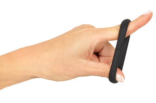 En hand med ljus hy håller Erecto Single Cock Ring, en svart flytande silikonring, runt pekfingret mot en vit bakgrund.