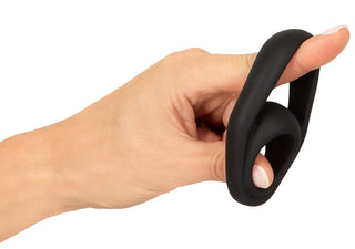 En hand håller Erecto Cock & Ball Ring, en populär sexleksak i svart silikon, mot en vit bakgrund.