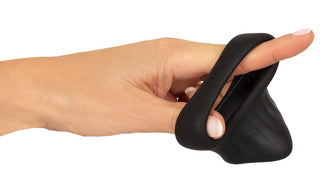 En hand håller Erecto Cock Ring Ball Stretcher, en kukring med dubbla öglor i svart flytande silikon, med en ögla runt pekfingret.