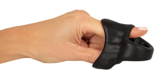 En hand sträcker ut Erecto Cock Ring Ball Stretcher, tillverkad av svart flytande silikon, med en tumme införd genom mitten.