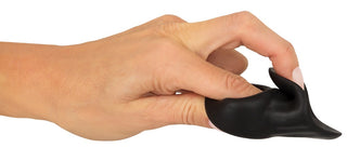 En hand klämmer och sträcker den svarta, flexibla Erecto Cock Ring Ball Stretcher tillverkad av flytande silikon mot en vit bakgrund.