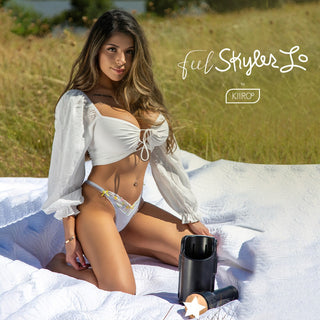 Kvinna i vit bikini och blus sitter på en filt utomhus med Feel Skyler Lo Masturbator Kiiroo placerad framför sig.