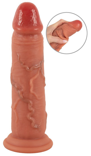 Realistixxx Real Skin Dildo har ett naturtroget utseende, detaljerade vener, en sugbas och ett flexibelt silikonskaft med dubbel densitet som visas i infällningen där den kläms.